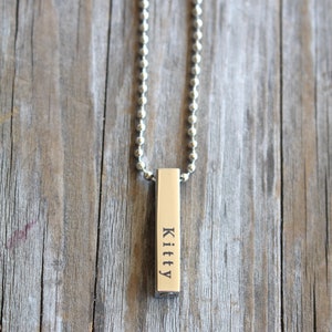 May include: A silver chain necklace with a silver bar pendant that says "Kitty" on it.