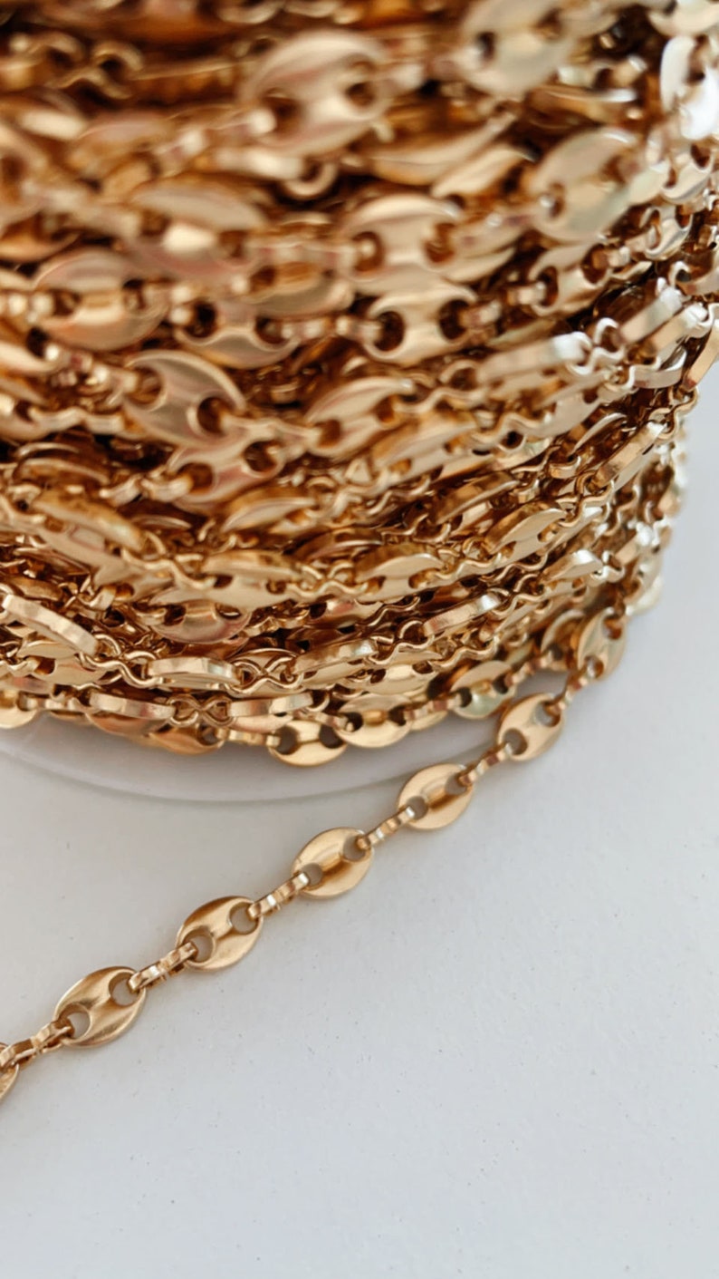 May include: A close-up of a gold chain with oval links. The chain is wound into a coil and a section of the chain is extended out to show the detail of the links.