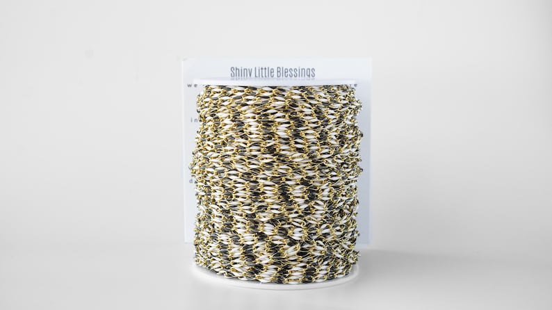 May include: A spool of gold and black chain trim with the words "Shiny Little Blessings" printed on the label.