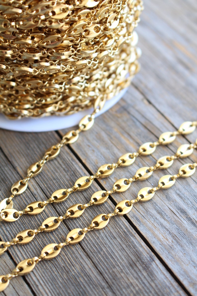 Op de afbeelding: Een spoel met een gouden ketting met ovale schakels. De ketting ligt in rijen op een houten oppervlak.