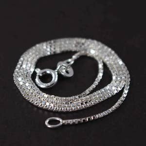 May include: A silver chain necklace with a box chain design. The chain is layered and has a lobster clasp closure.