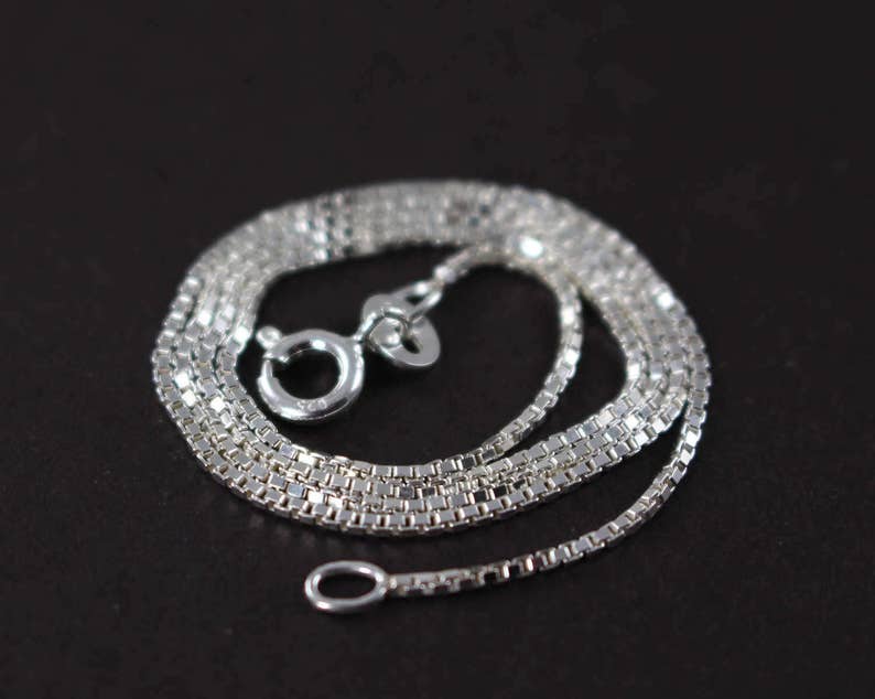 May include: A silver chain necklace with a box chain design. The chain is layered and has a lobster clasp closure.