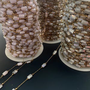 May include: Spools of beaded chain in three colors: pale pink, bronze, and iridescent white. The beads are rectangular and strung on gold-colored wire. The spools are on white cardboard spools.