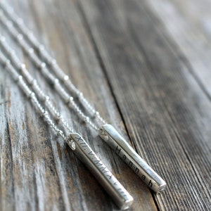 May include: Two silver necklaces with personalized bar pendants. One pendant reads "Hannah" and the other reads "XI.V.MMXVII".