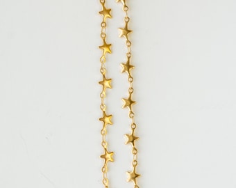 May include: Two strands of gold-colored star-shaped chain. The chains are vertically aligned against a white background. The stars are evenly spaced and connected by small links, creating a delicate and celestial design.