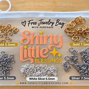 May include: A translucent plastic zipper pouch containing various metal jump rings. The bag features the text "Free Jewelry Bag WITH PURCHASE" and "Shiny little BLESSINGS" with "WWW.SHINYLITTLEBLESSINGS.COM". Labels indicate Gold 5.5mm, Gold 7.5mm, Silver 5.5mm, White Silver 5.5mm, and Silver 7.5mm.