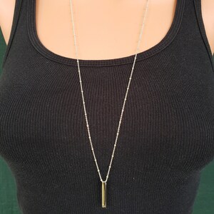 May include: A silver chain necklace with a long, thin, silver bar pendant.