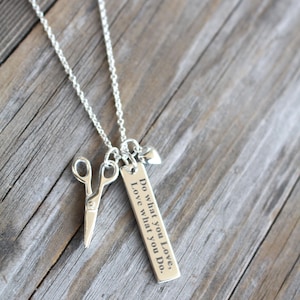 May include: A silver necklace with a charm that says "Do what you love, Love what you do." The charm is attached to a silver chain with a pair of silver scissors and a small silver heart.