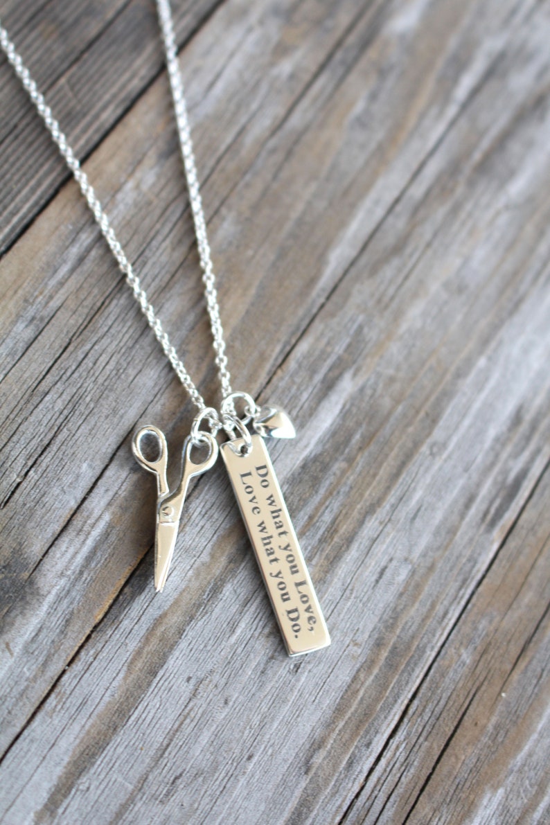 May include: A silver necklace with a charm that says "Do what you love, Love what you do." The charm is attached to a silver chain with a pair of silver scissors and a small silver heart.