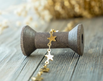 May include: A gold chain with star-shaped charms draped over a wooden spool. The spool is on a rustic wooden surface.