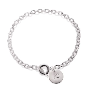 Puede incluir: Un collar de cadena de plata con cierre de palanca y un dije redondo con la letra "K" grabada.