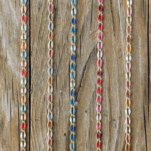 May include: Six strands of colorful, beaded necklaces on a wooden background. Each necklace is made of small, oval-shaped beads in various shades of red, pink, blue, green, and white.