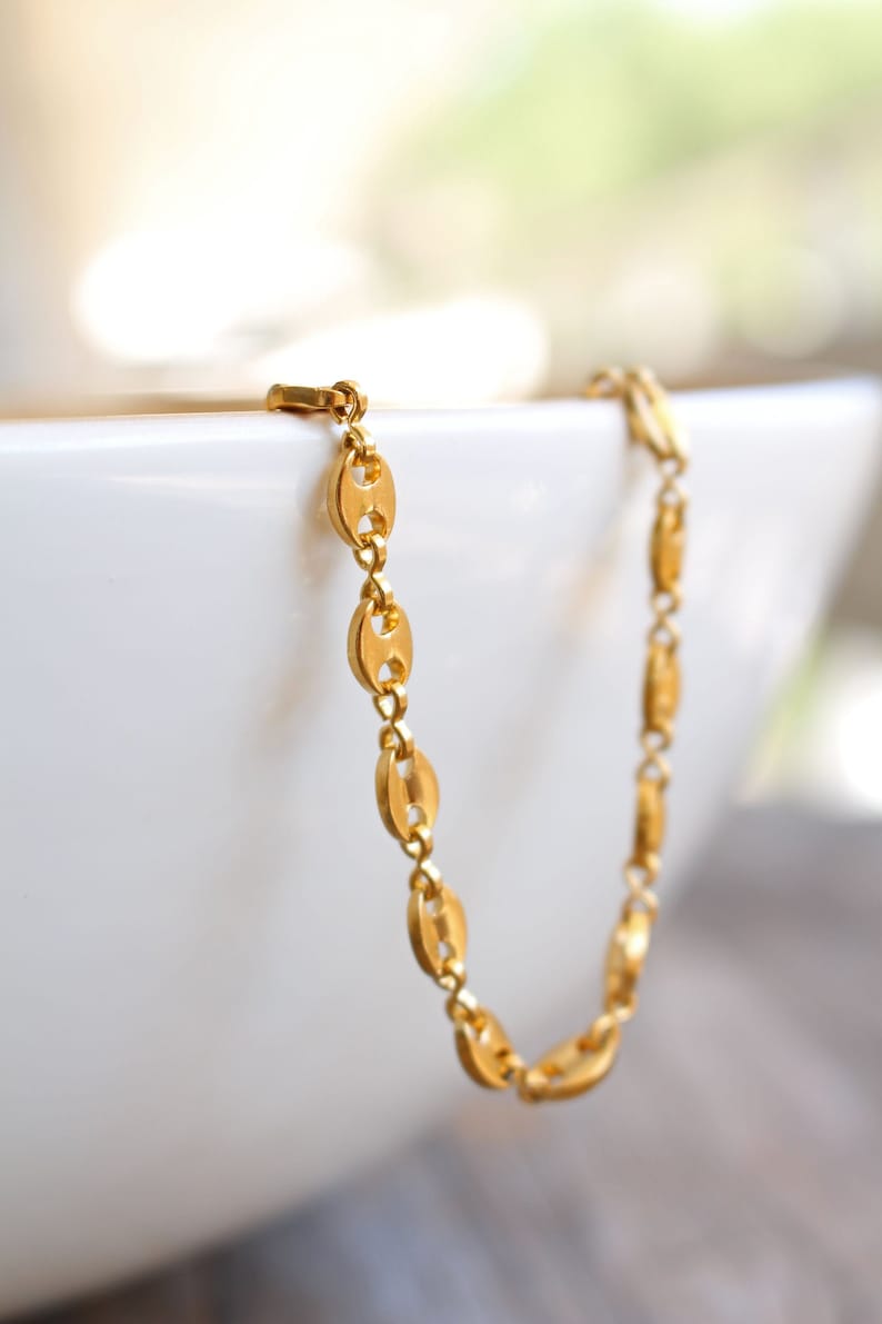 May include: A gold chain bracelet with a mariner link design. The bracelet is on a white surface.