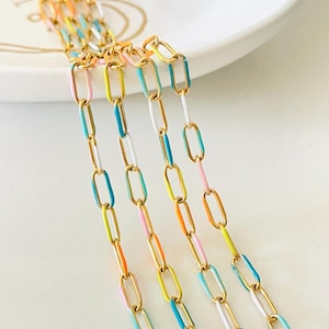 Op de afbeelding: Een close-up van vijf gouden kettingen met kleurrijke emaille accenten. De kettingen zijn verticaal gerangschikt en allemaal even lang. De emaille accenten zijn in tinten blauw, groen, roze en geel.