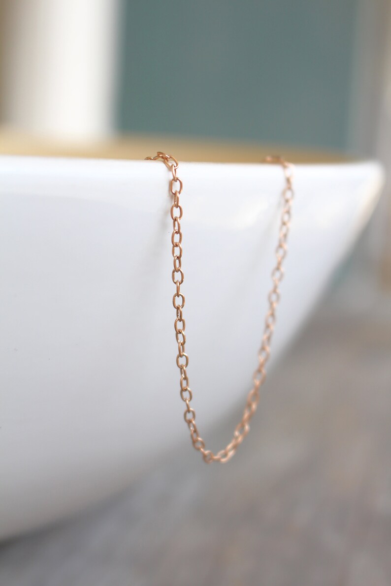 May include: A delicate rose gold chain necklace. The chain is made of small, linked oval shapes.