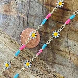 May include: Gold-toned chain necklaces with daisy flower charms and colorful beads in pink and blue. The necklaces are displayed on a wooden surface, with a penny for scale.