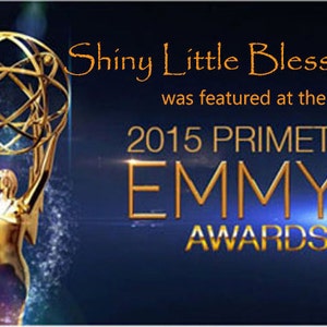 May include: A gold statuette of a woman holding a golden globe with a starburst design. The text "Shiny Little Blessings was featured at the 2015 Primetime Emmy Awards" is displayed above the statuette.