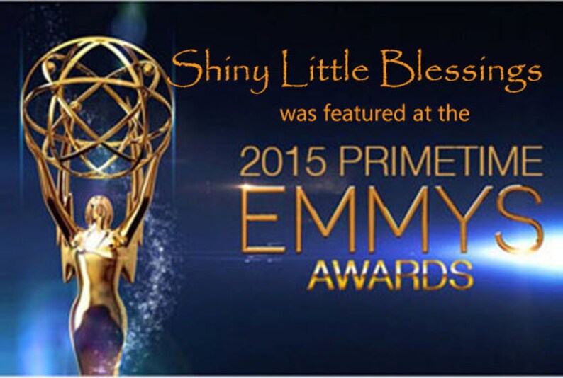May include: A gold statuette of a woman holding a golden globe with a starburst design. The text "Shiny Little Blessings was featured at the 2015 Primetime Emmy Awards" is displayed above the statuette.