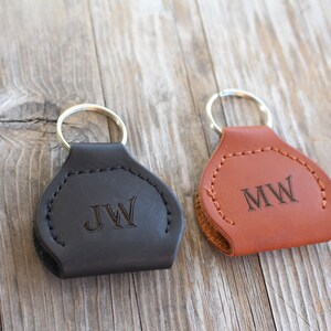 May include: Two leather keychains with metal rings. The keychain on the left is black with the initials "JW" engraved on it. The keychain on the right is brown with the initials "MW" engraved on it.