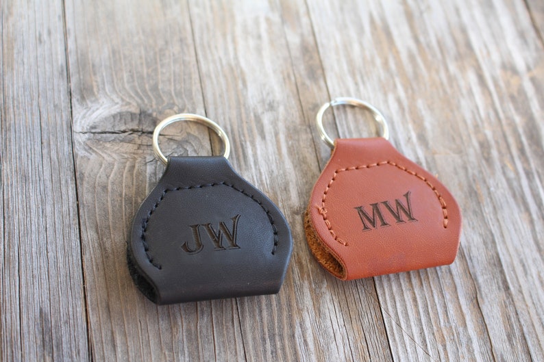 May include: Two leather keychains with metal rings. The keychain on the left is black with the initials "JW" engraved on it. The keychain on the right is brown with the initials "MW" engraved on it.