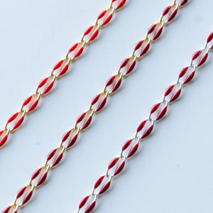 May include: Three gold chains with red enamel accents. The chains are arranged in a diagonal pattern on a white background.