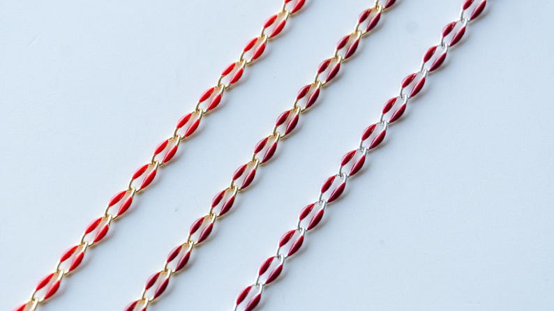 May include: Three gold chains with red enamel accents. The chains are arranged in a diagonal pattern on a white background.