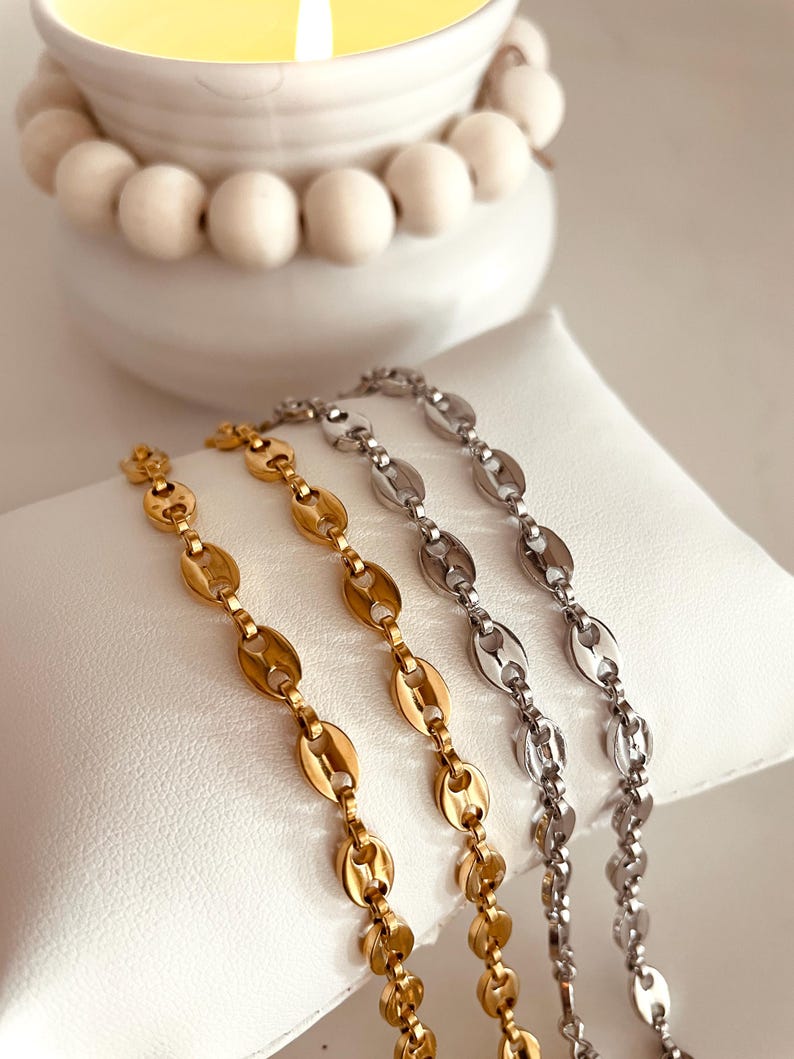 Op de afbeelding: Drie gouden, zilveren en ros&eacute;gouden kettingen met een ankerketting ontwerp. De kettingen liggen op een wit oppervlak.