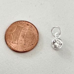 May include: A small silver charm with a clear round crystal stone. The charm is about the size of a US penny.