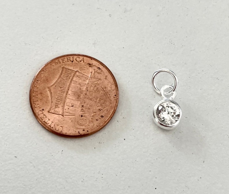 May include: A small silver charm with a clear round crystal stone. The charm is about the size of a US penny.
