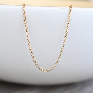 May include: A gold chain necklace with a delicate, oval-shaped link pattern. The chain is displayed on a white surface.
