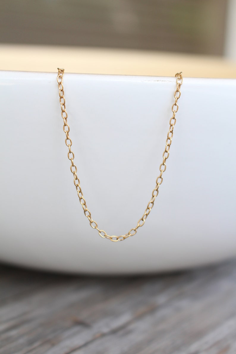 May include: A gold chain necklace with a delicate, oval-shaped link pattern. The chain is displayed on a white surface.
