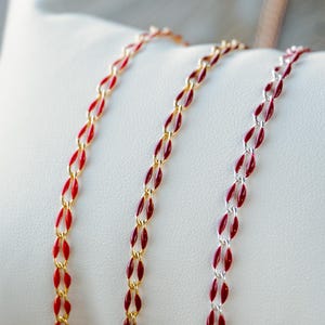 May include: Three gold, silver, and red chains with red enamel accents. The chains are laid out on a white surface.