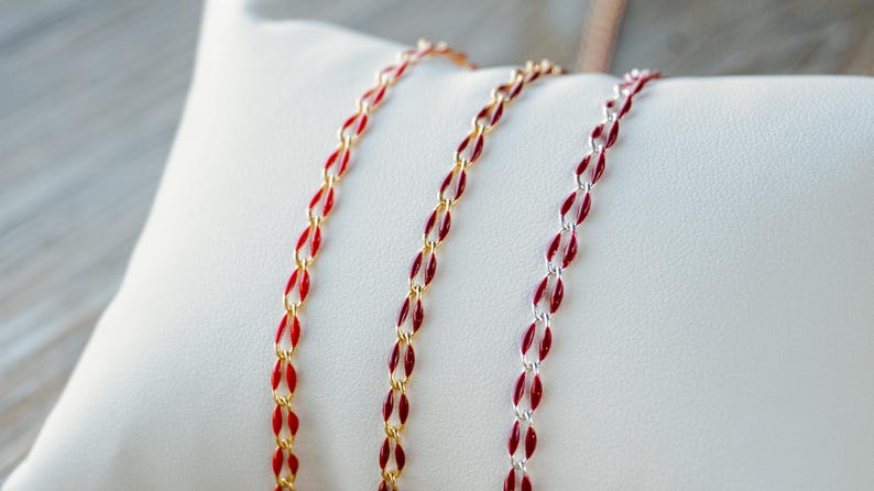 May include: Three gold, silver, and red chains with red enamel accents. The chains are laid out on a white surface.