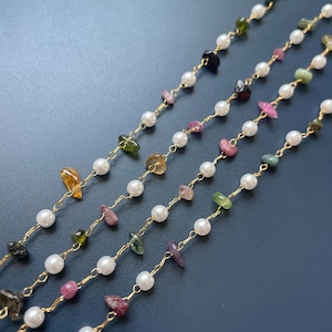 Puede incluir: Primer plano de cuatro hilos de joyer&iacute;a delicada. Cada hilo presenta peque&ntilde;as piedras preciosas de colores y perlas blancas ensartadas en una cadena dorada. Las piedras preciosas son de varios colores, incluyendo verde, rosa y amarillo. El fondo es azul oscuro.