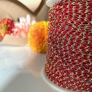 May include: A spool of red and gold chain. The chain is made of small, oval-shaped links. The chain is wound tightly around the spool.