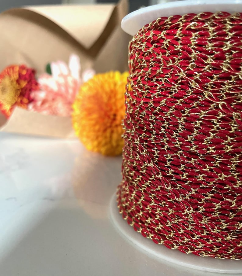 May include: A spool of red and gold chain. The chain is made of small, oval-shaped links. The chain is wound tightly around the spool.
