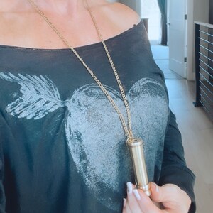 K&ouml;nnte beinhalten: Eine goldene Kettenkette mit einem Messingr&ouml;hrenanh&auml;nger. Die Kette wird von einer Person getragen, die ein schwarzes, schulterfreies Hemd mit einem wei&szlig;en Herzdesign tr&auml;gt.