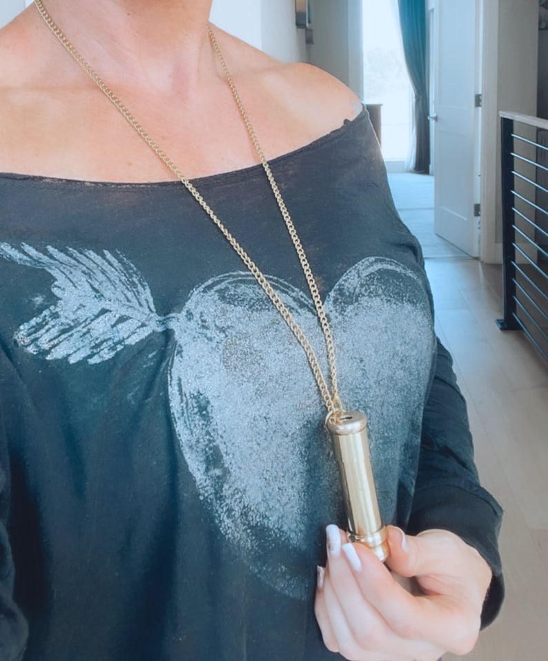 K&ouml;nnte beinhalten: Eine goldene Kettenkette mit einem Messingr&ouml;hrenanh&auml;nger. Die Kette wird von einer Person getragen, die ein schwarzes, schulterfreies Hemd mit einem wei&szlig;en Herzdesign tr&auml;gt.