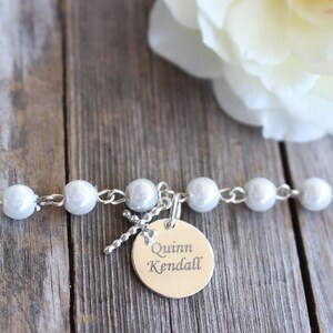 May include: A white pearl bracelet with a silver charm that says "Quinn Kendall" on a wooden background.