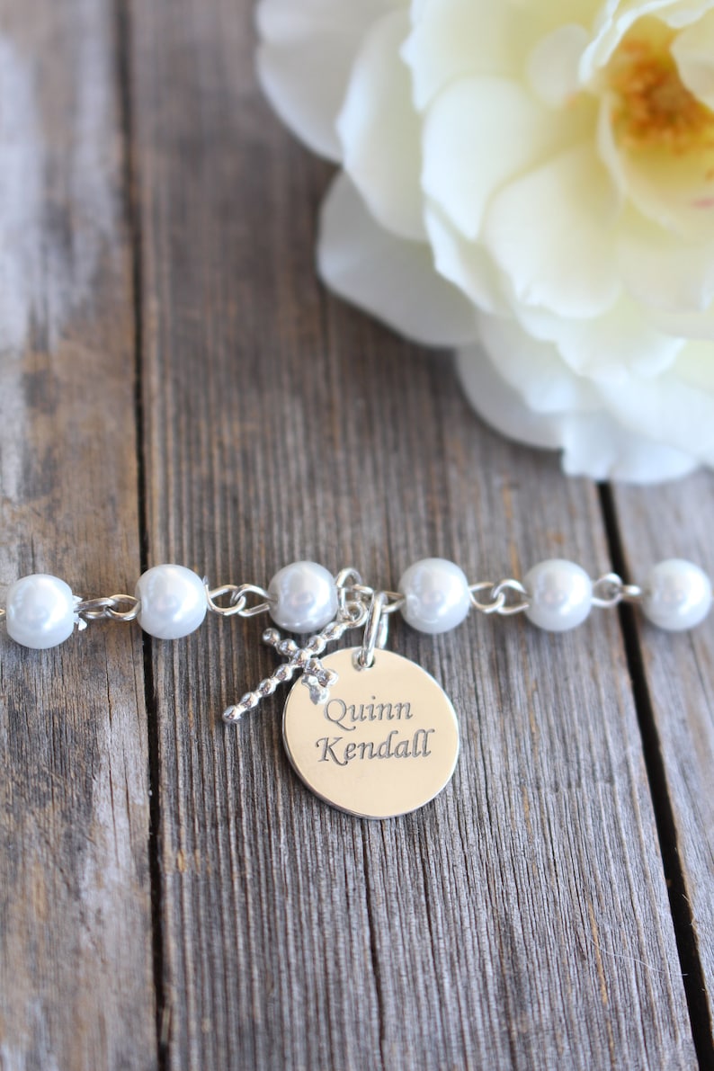 May include: A white pearl bracelet with a silver charm that says "Quinn Kendall" on a wooden background.
