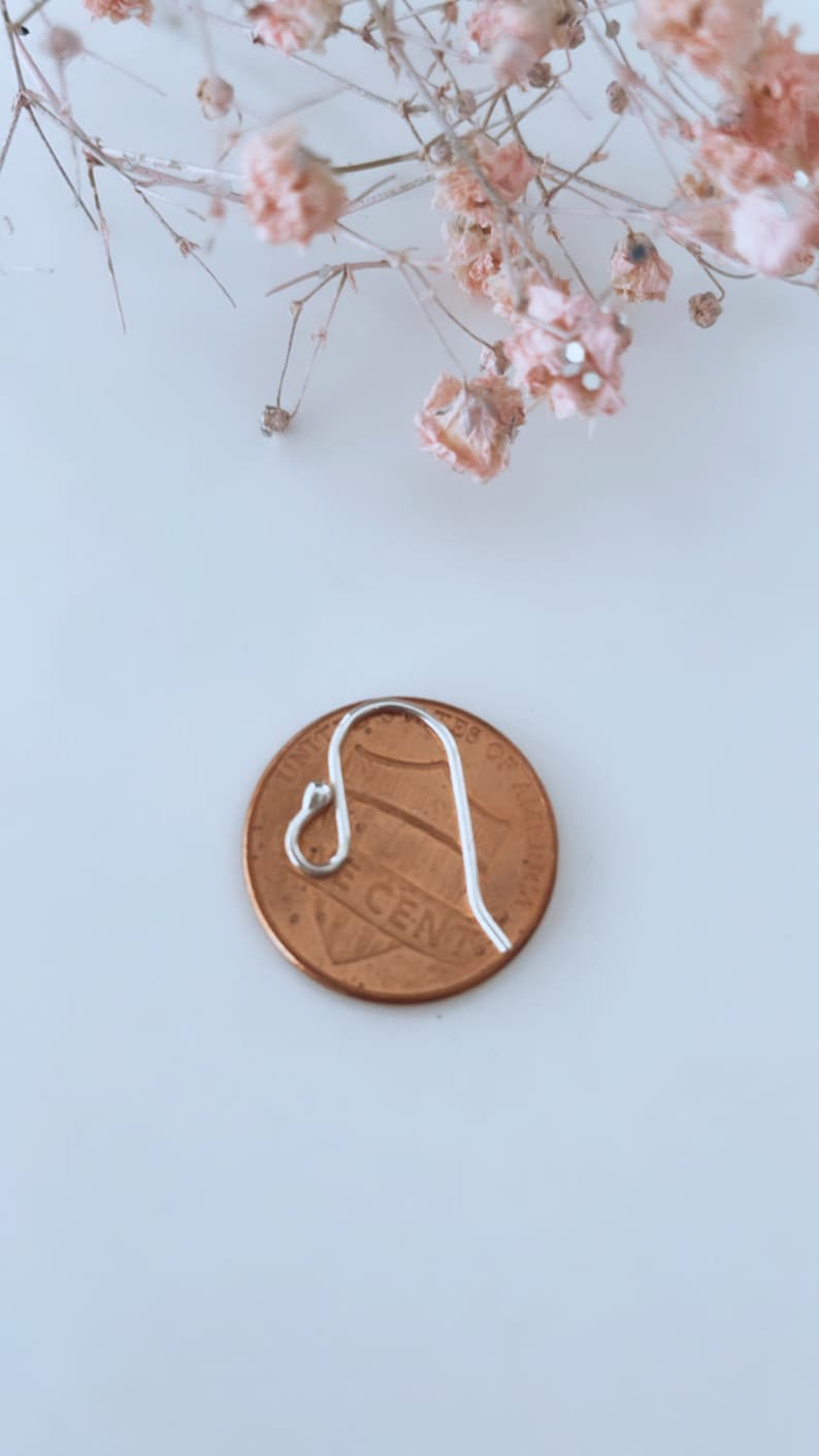 May include: A silver earring hook next to a US penny. The hook is about the size of the penny.