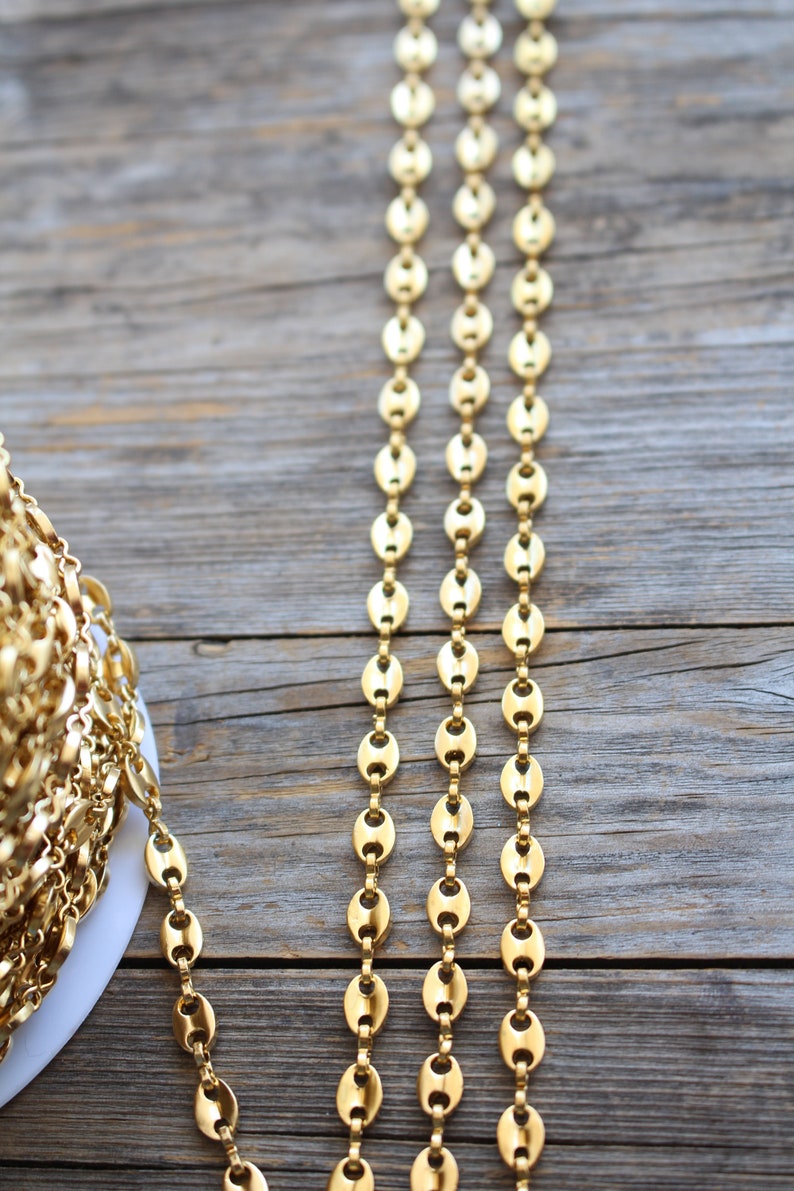 Op de afbeelding: Drie strengen van een gouden ovale ketting, plat liggend op een houten oppervlak.
