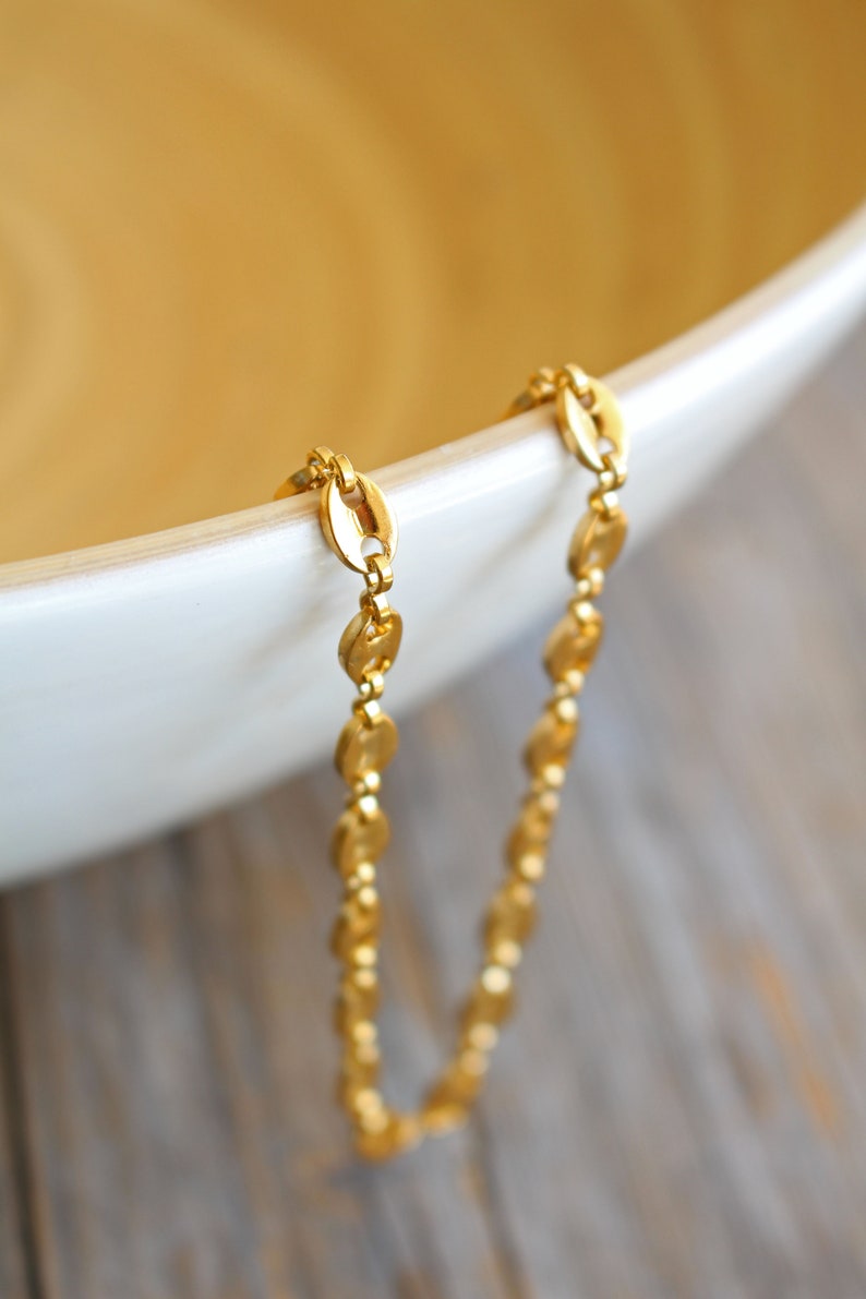 May include: A gold chain necklace with a delicate, oval-shaped link design. The chain is draped over the edge of a white bowl.