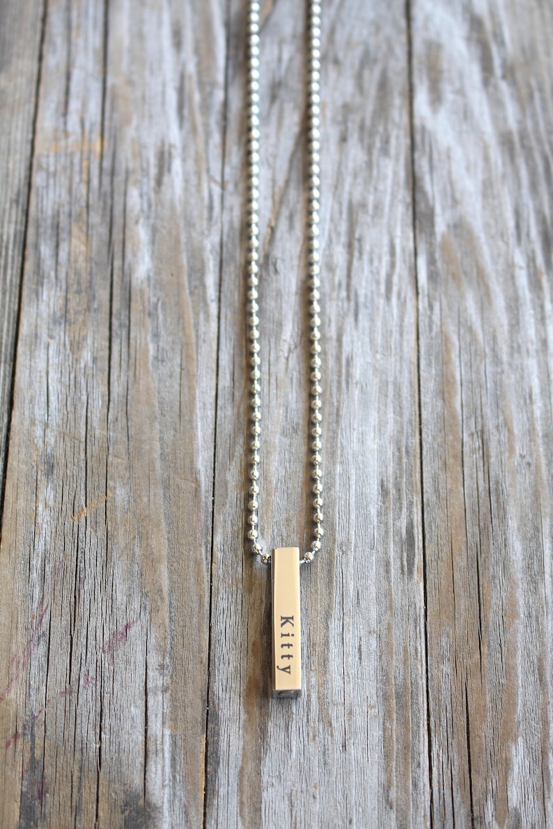 May include: A silver chain necklace with a silver bar pendant engraved with the name "Kitty".