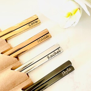 May include: Four pairs of personalized chopsticks in gold, rose gold, silver, and black. The chopsticks are engraved with the names Cora, Malia, Rachel, and Skyla.