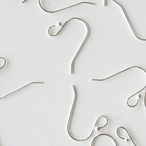 May include: A close-up of silver earring hooks with a small ball at the end of each hook.