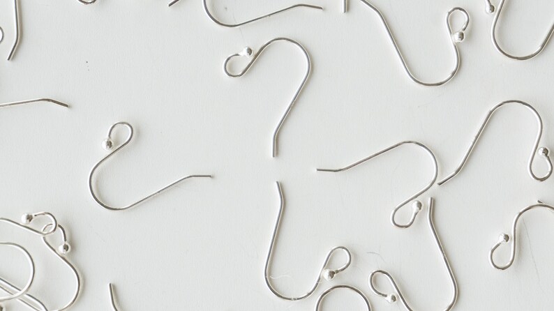 May include: A close-up of silver earring hooks with a small ball at the end of each hook.