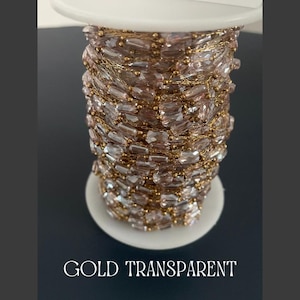 May include: A spool of gold-colored chain with transparent, rectangular beads. The chain is wound around a white spool. The text "GOLD TRANSPARENT" is at the bottom of the image.