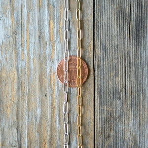 May include: Three silver and gold chains laid out on a wooden surface. A penny is placed between the chains.