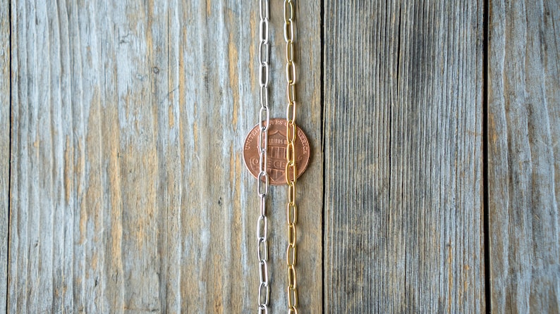 May include: Three silver and gold chains laid out on a wooden surface. A penny is placed between the chains.